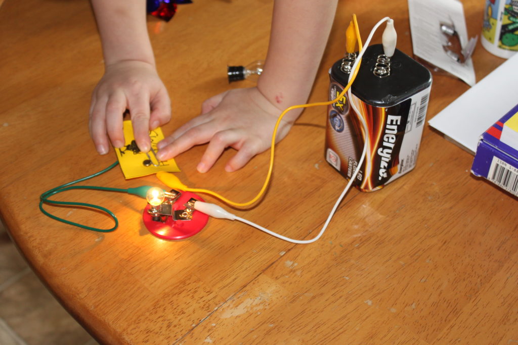 A child pushing down on a paperclip to turn on a light in a simple electrical experiment.